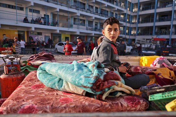 Палестинский мальчик, бежавший из дома из-за израильских ударов, сидит на матрасе снаружи в школе, принимающей беженцев (14 мая 2021). Газа - Sputnik Армения
