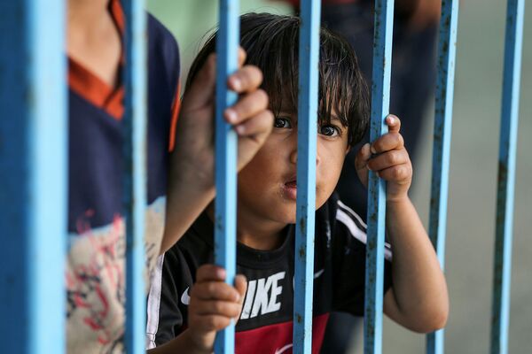 Палестинский мальчик, бежавший из дома из-за израильских ударов, смотрит через перила в сторону школы, принимающей беженцев (15 мая 2021). Газа - Sputnik Армения