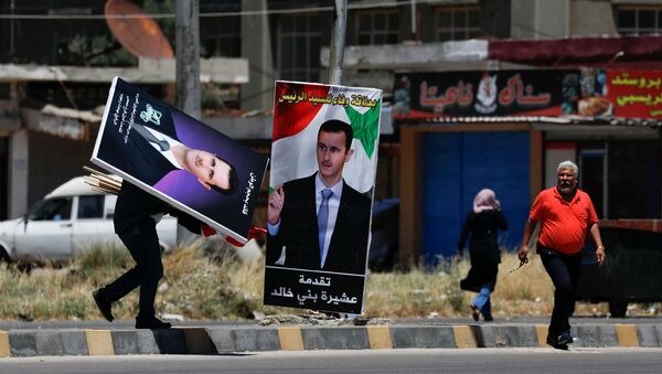 Мужчина идет с плакатами с изображением президента Сирии Башара аль-Асада в преддверии президентских выборов 26 мая в районе Аль-Ваер в Хомсе - Sputnik Армения