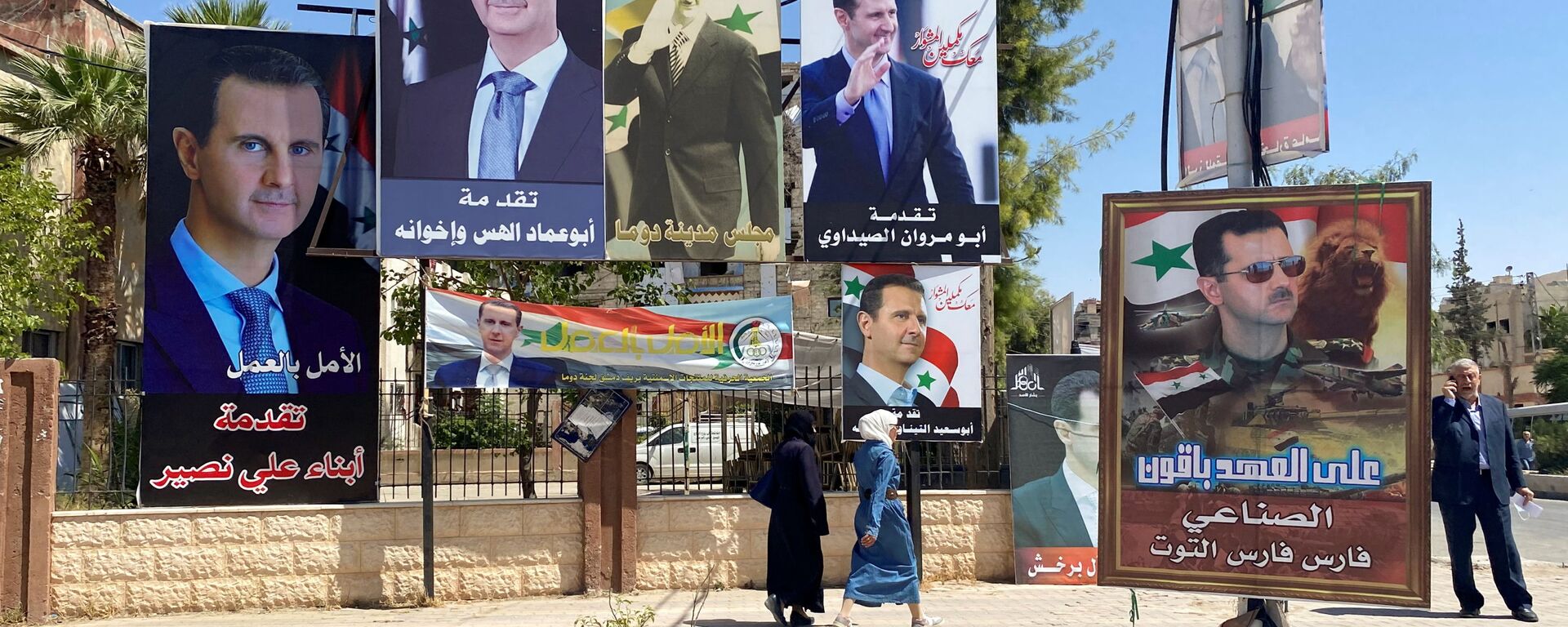 Женщины проходят возле плакатов с изображением президента Сирии Башара аль-Асада во время президентских выборов - Sputnik Армения, 1920, 22.12.2021