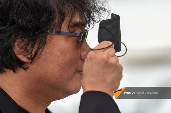 Южнокорейский режиссер Бонг Джун Хо держит перед глазами медицинскую маску во время фотосессии на 74-м международном кинофестивале в Каннах  - Sputnik Армения