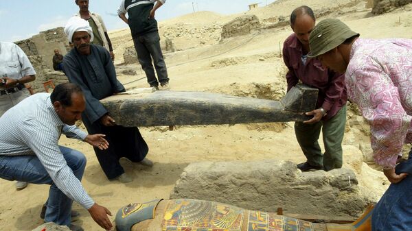 Археологи держат деревянный гроб с ярко окрашенной и позолоченной мумией во время раскопок в Саккаре - Sputnik Армения
