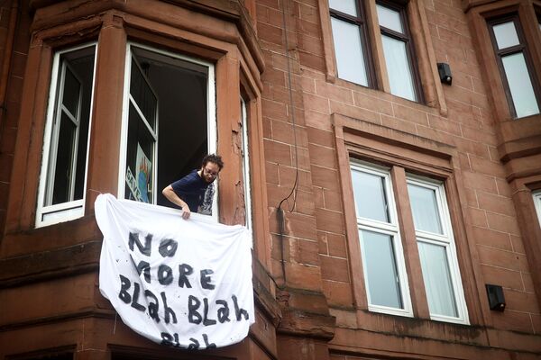 Мужчина вывешивает из окна плакат с надписью &quot;Хватит бла-бла-бла&quot; в поддержку акции протеста во время Конференции ООН по изменению климата (COP26) в Глазго. - Sputnik Армения
