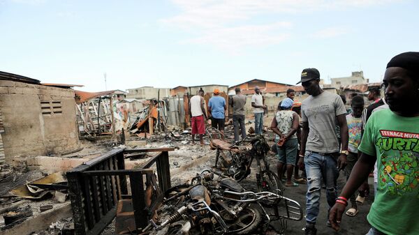 Люди стоят среди останков сгоревших мотоциклов и бедных жилищ, которые были разрушены в результате взрыва бензовоза в районе Кап-Аитьена (14 декабря 2021). Гаити - Sputnik Армения