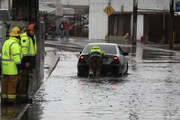 Пожарный помогает застрявшему водителю на одной из улиц Лос-Анджелеса во время сильного шторма, обрушившегося на Калифорнию с дождем и затоплением улиц. - Sputnik Армения