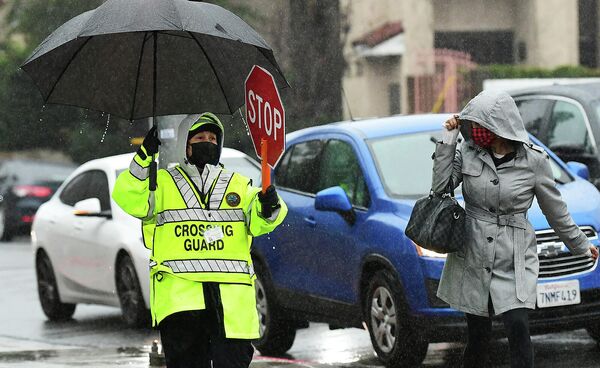 Охранник на школьном переходе держит знак остановки для движения автомобилей во время шторма в Калифорнии  - Sputnik Армения