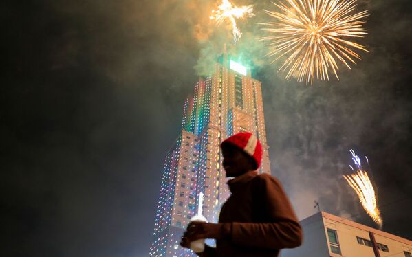Прохожий на фоне фейерверка над Старой башней UAP во время празднования Нового года в Найроби, Кения, 1 января 2022 года - Sputnik Армения