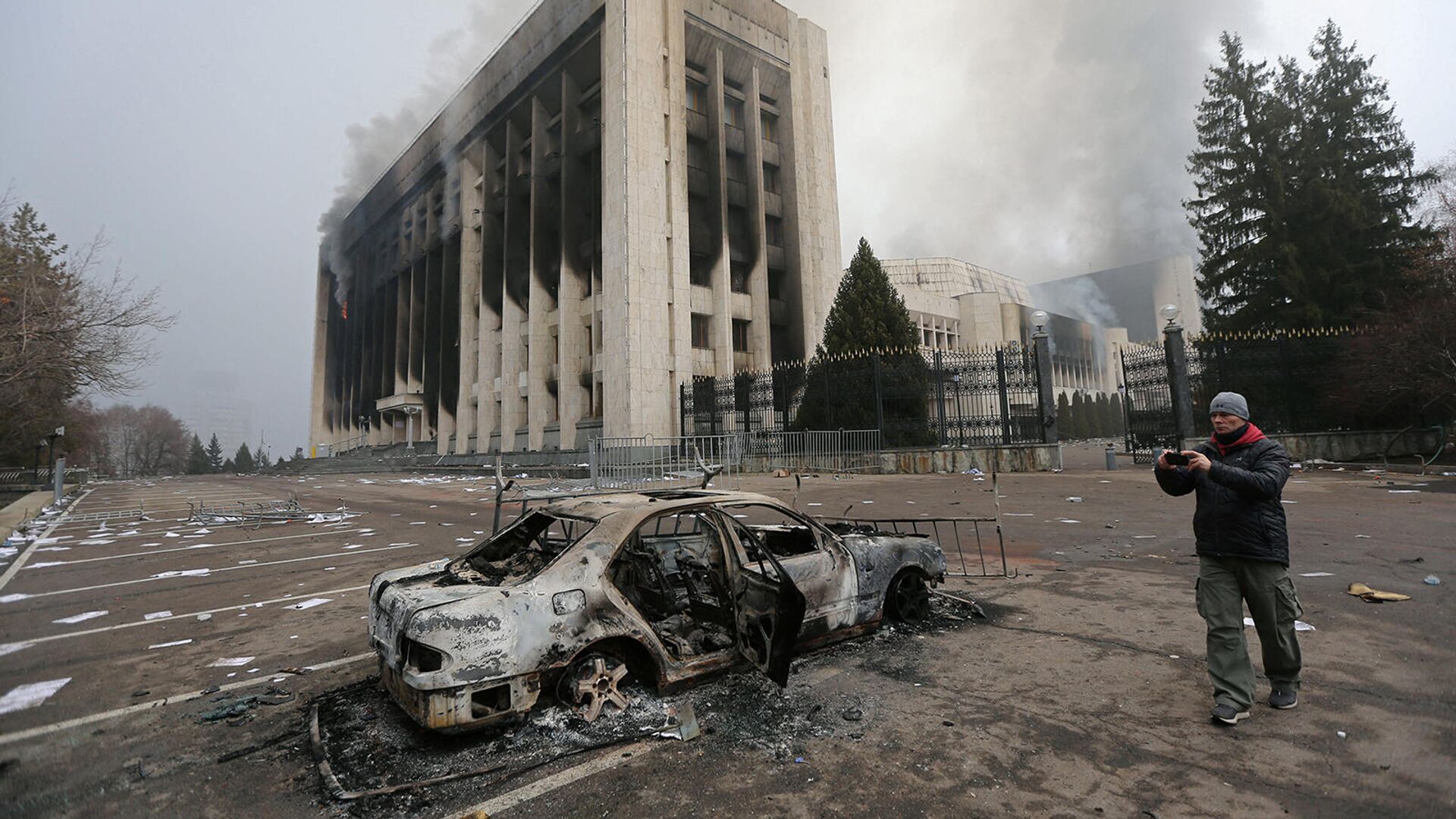 Мужчина фотографирует сгоревший автомобиль перед зданием мэрии Алматы (6 января 2022). Казахстан - Sputnik Армения, 1920, 07.01.2022