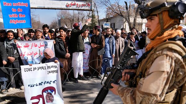 Боец движения Талибан рядом с протестующими во время митинга, осуждающего президента США Джо Байдена (15 февраля 2022). Кабул - Sputnik Армения