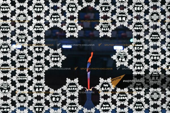 Факел в проеме узора в виде снежинки. Фон составляют также снежинки с названиями стран-участниц Олимпиады - Sputnik Армения