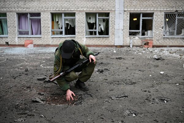 Сотрудник народной милиции ДНР возле воронки от снаряда у школы Горловки - Sputnik Армения