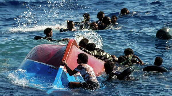 Мигранты рядом с перевернутой деревянной лодкой во время кораблекрушения у острова Лампедуза - Sputnik Армения