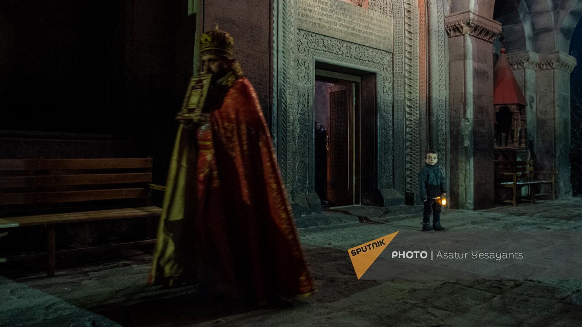 Мальчик с лампадкой Чрагалуйца смотрит вслед священнику в церкви Сурб Геворг (5 января 2023). село Мугни - Sputnik Армения, 1920, 31.05.2023