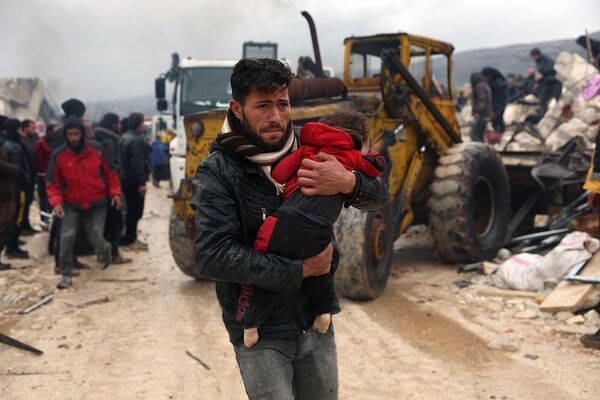 Мужчина несет пострадавшего от землетрясения ребенка в деревне Бесния. Сирия, провинция Идлиб - Sputnik Армения