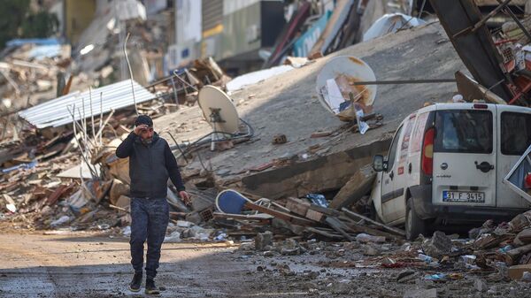 Мужчина проходит мимо обломков разрушенных зданий в Антакье (21 февраля 2023). Турция - Sputnik Армения