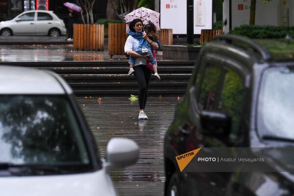 Молодая женщина с ребенком на руках под дождем на одной улиц в Ереване - Sputnik Армения
