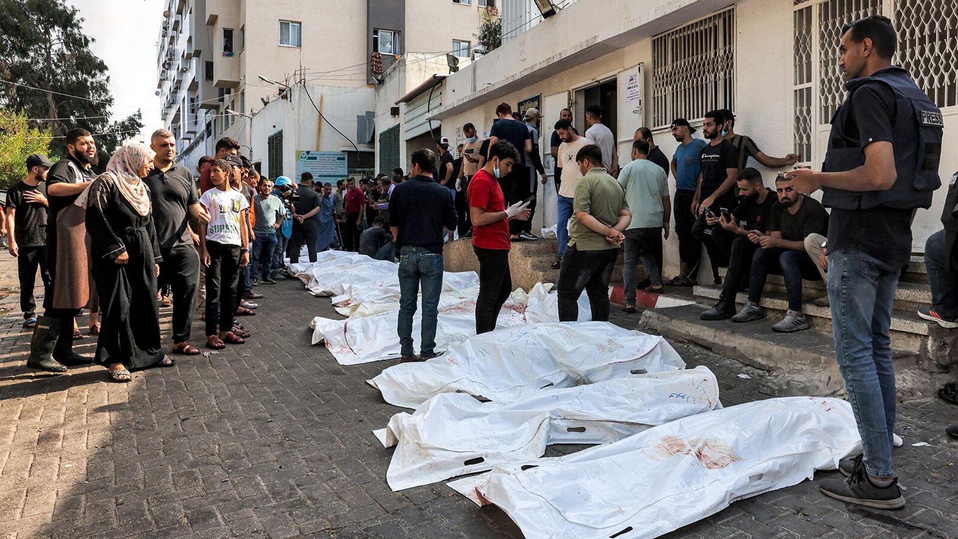 Люди стоят у тел жертв израильских авиаударов возле морга больницы аль-Шифа (12 октября 2023). Газа - Sputnik Армения, 1920, 18.10.2023