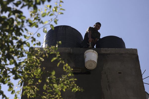 Տղամարդը ջրով լի դույլ է բարձրացնում տանիք, որպեսզի լրացնի Գազայի հարավում գտնվող Ռաֆահ փախստականների ճամբարի ջրի պաշարները: - Sputnik Արմենիա