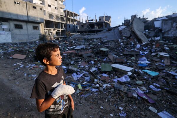 Վիրավոր պաղեստինցի տղան նայում է իսրայելական ավիահարվածների ժամանակ ավերված շենքերին՝ Գազայի հարավում գտնվող Ռաֆահ փախստականների ճամբարից ոչ հեռու: - Sputnik Արմենիա
