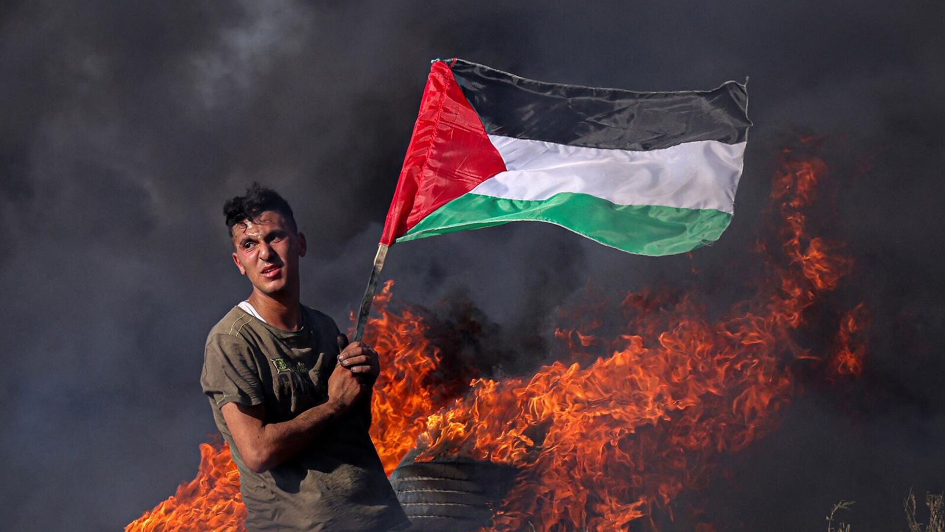 Палестинский юноша сжигает шины во время акции протеста у пограничного забора с Израилем (3 июля 2023). Газа  - Sputnik Армения, 1920, 26.10.2023