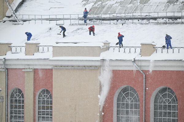 Сотрудники коммунальных служб расчищают крышу дома во время снегопада в Москве - Sputnik Армения