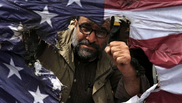 Иранский протестующий сжимает кулак за сожженным изображением флага США во время собрания после пятничной молитвы (11 мая 2018). Тегеран - Sputnik Армения