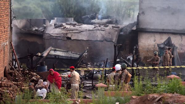 Жители сидят среди обломков своего разрушенного дома около оцепленного солдатами места крушения военного самолета (30 июля 2019). Равалпинди, Пакистан - Sputnik Արմենիա