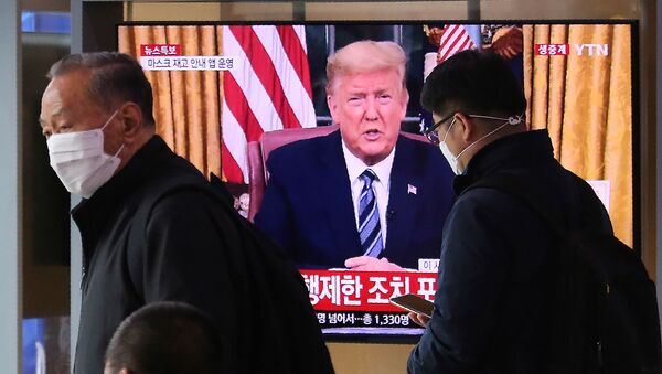 Люди в масках проходят перед телевизионным экраном, на котором в прямом эфире демонстрируется выступление президента США Дональда Трампа (12 марта 2020). Сеул - Sputnik Արմենիա