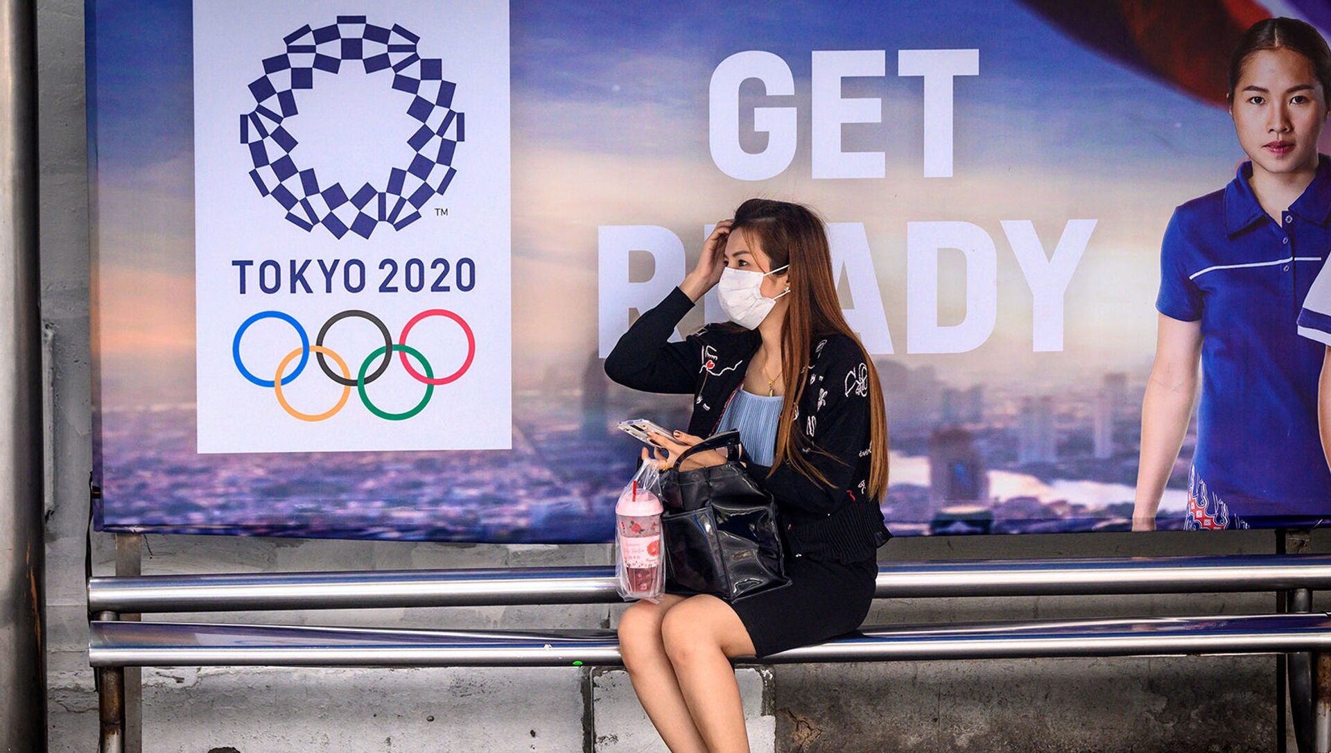Женщина в защитной маске на автобусной остановке перед рекламой Олимпийских игр Токио-2020 (16 марта 2020). Бангкок - Sputnik Армения, 1920, 18.03.2021