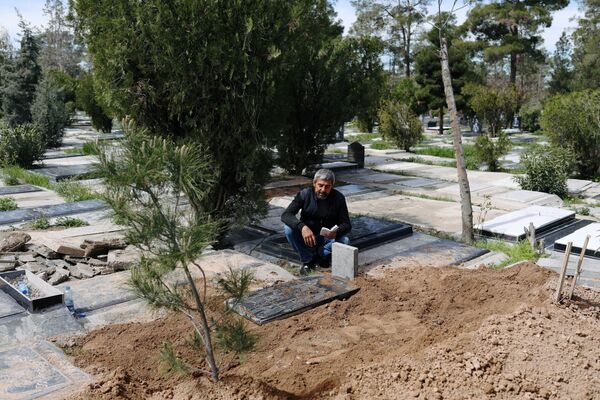 Родственник скончавшегося от коронавируса журналиста Абдоллы Завье читает Коран после похорон на кладбище Бехешт-Захра (24 марта 2020). Тегеран - Sputnik Армения