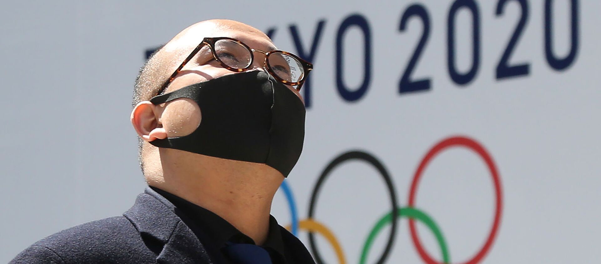 Мужчина в защитной маске проходит перед логотипом токийской Олимпиады (25 марта 2020). Токио - Sputnik Армения, 1920, 31.07.2021