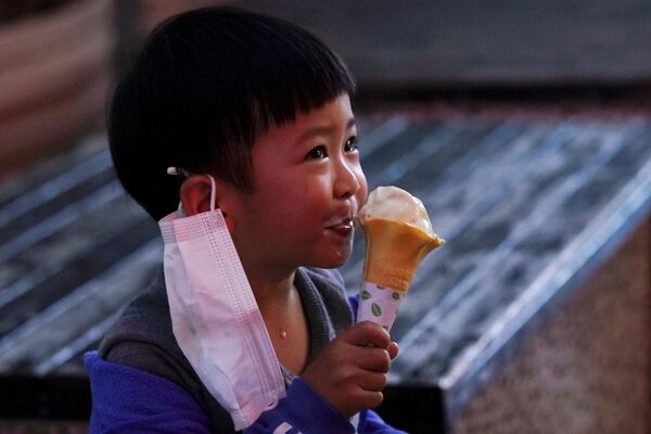 Ребенок с медицинской маской ест мороженое в первый день открытия магазина в Сяньнин, Китай - Sputnik Армения