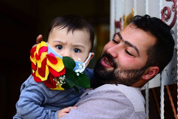 Мужчина с ребенком в украшенной цветами защитной маске в Эн-Наджафе, Ирак - Sputnik Армения