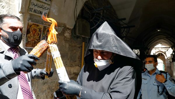 Армянский священник в защитной маске и перчатках передает Благодатный огонь, зажженный в храме Гроба Господня (18 апреля 2020). Иерусалим - Sputnik Արմենիա