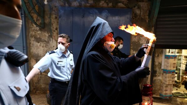 Армянский священник в защитной маске и перчатках держит Благодатный огонь, зажженный в храме Гроба Господня (18 апреля 2020). Иерусалим
 - Sputnik Армения