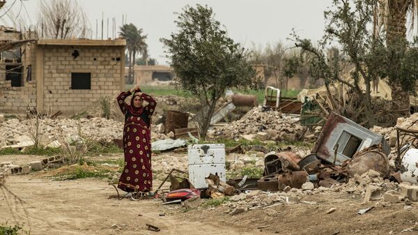 Женщина в платке рядом с останками разрушенного дома в восточной сирийской деревне Багхуз в провинции Дейр-эз-Зор (13 марта 2020). - Sputnik Армения